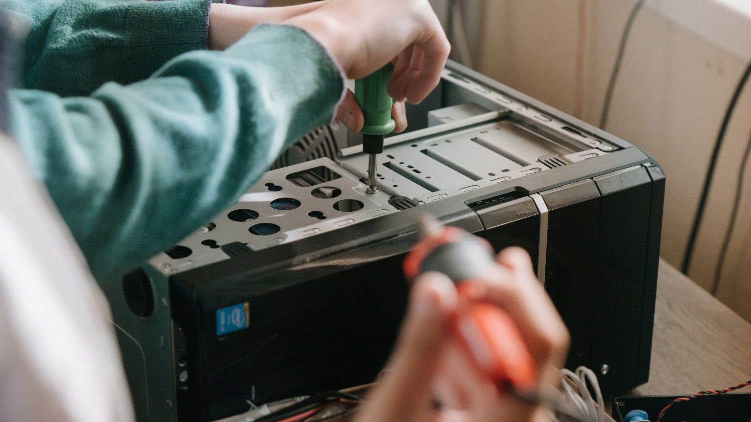 One person removing a screw from a computer and another holding a soldering iron