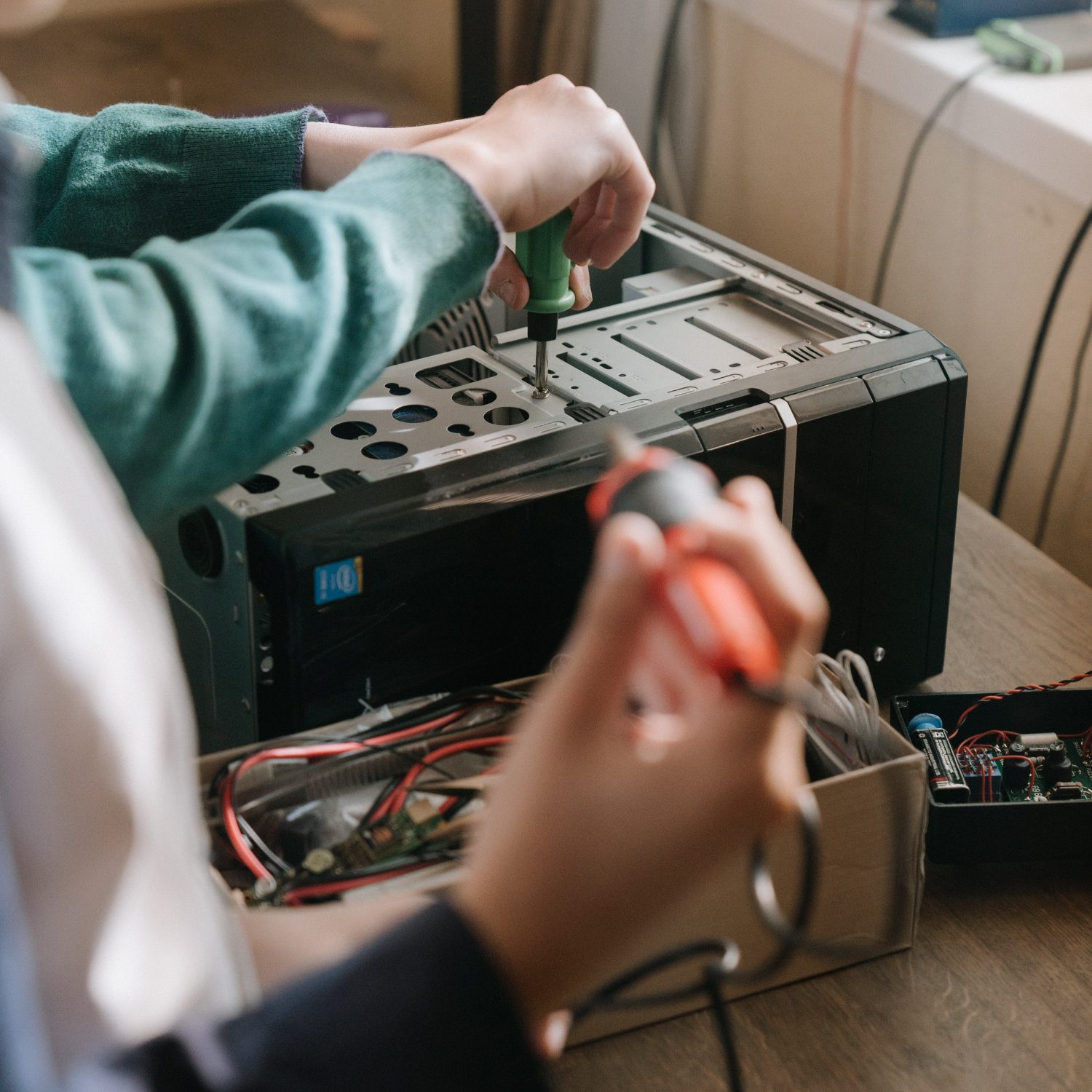 One person removing a screw from a computer and another holding a soldering iron